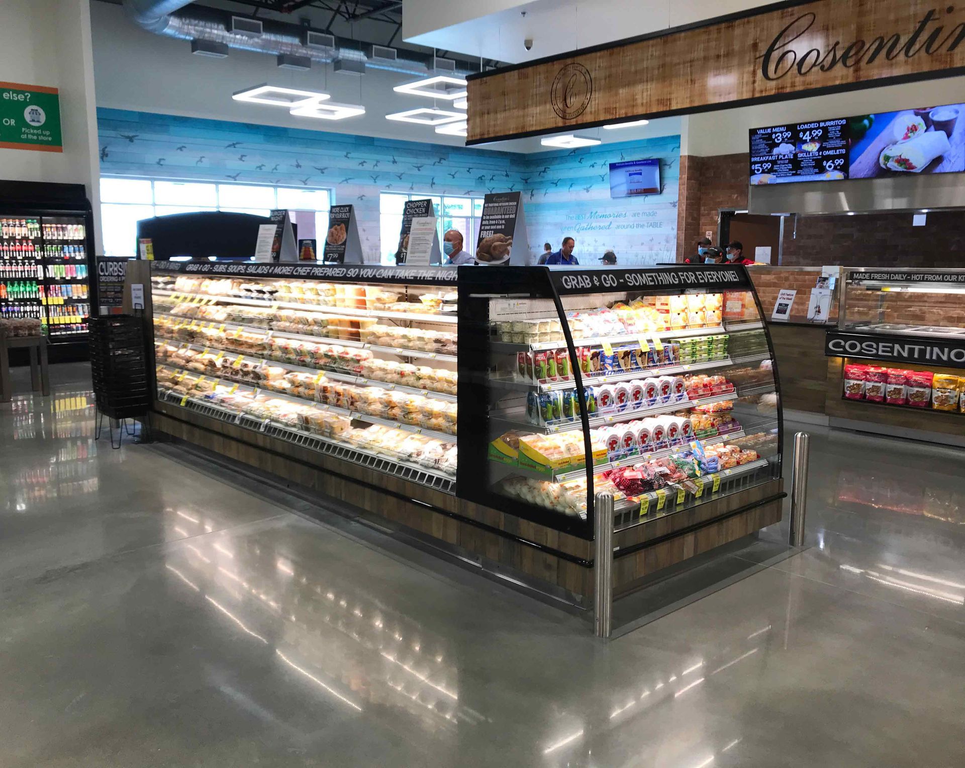 Deli section in a grocery store. Refrigerated display cases filled with prepared food, under bright lighting.