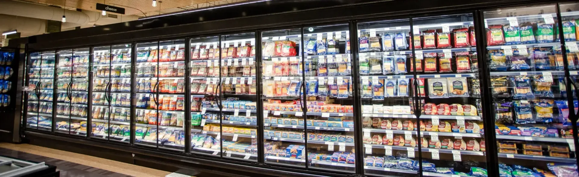 A long row of refrigerated glass doors at a grocery store, filled with various packaged food products.