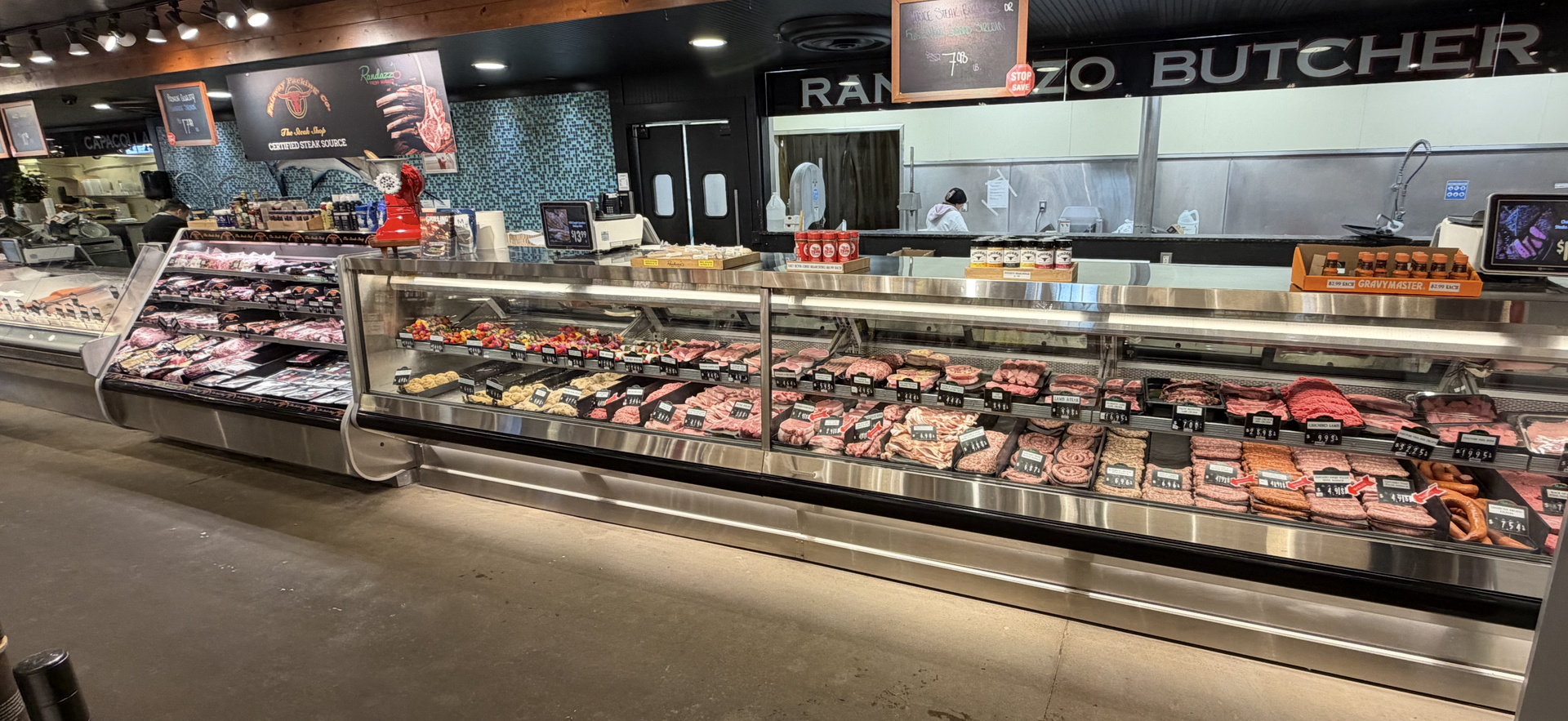 Meat display case inside a butcher shop. Sliced and packaged meats are visible, along with staff in the background.