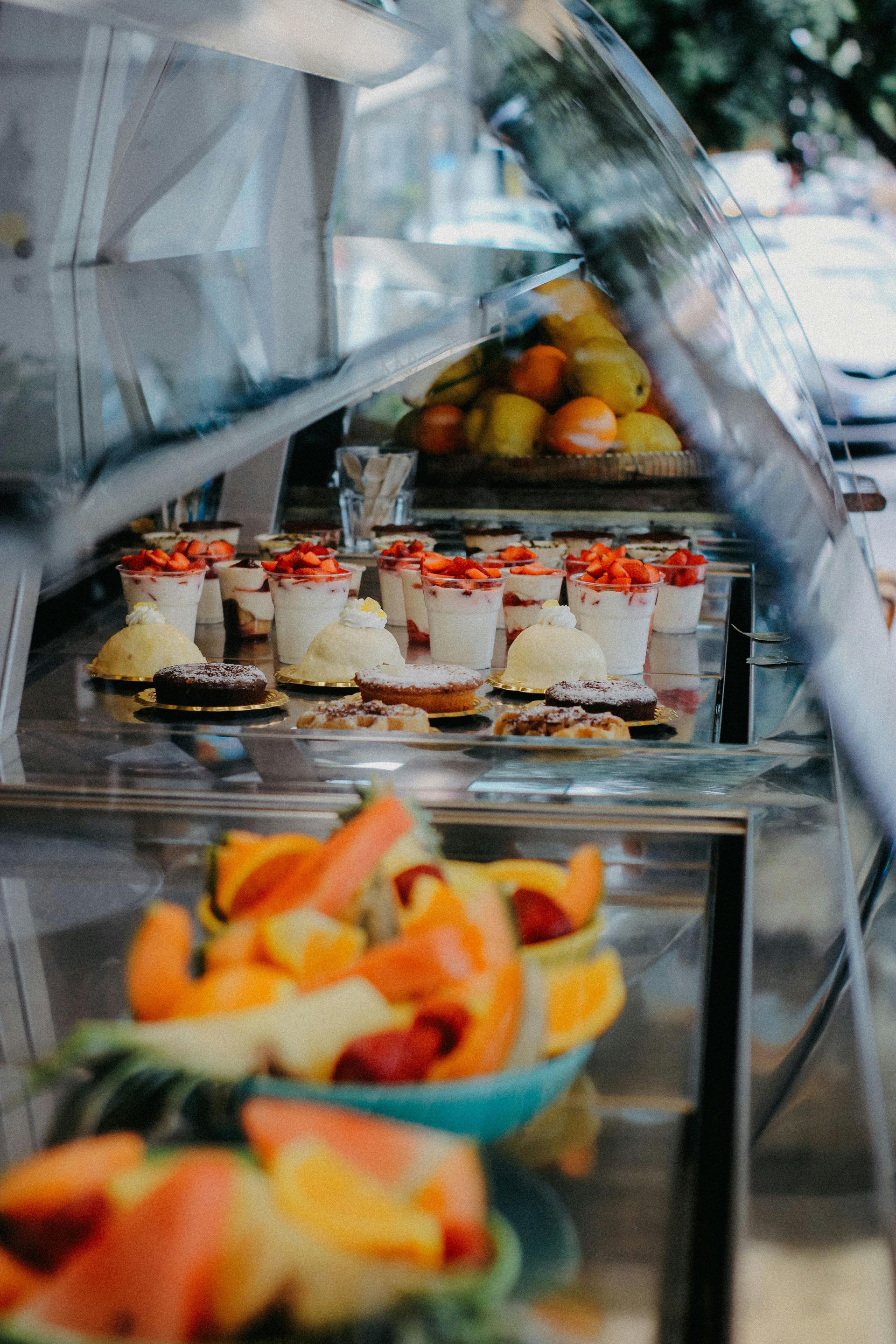 Display case with fruit: sliced melon, fruit salad, strawberry desserts, oranges.
