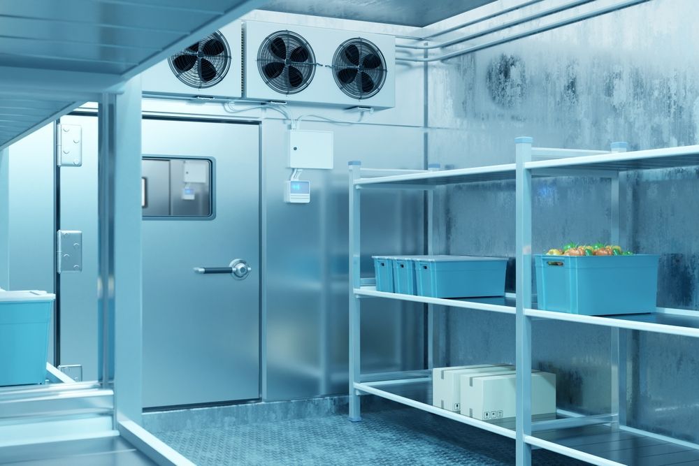 Cold storage room interior with metal shelving, blue bins, a door, and cooling fans.