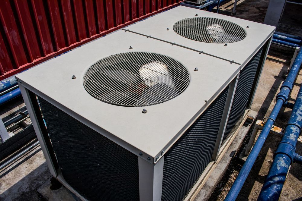 Rooftop air conditioning unit with two circular fan vents, silver casing, and blue piping.