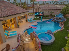 Resort pool with waterslides, hot tub, lounge chairs, and colorful floats beside villas