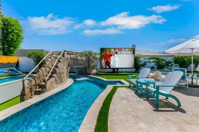 Resort pool with stone bridge, lounge chairs, and blue sky on a sunny day