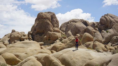 Person in a red shirt standing among large desert boulders under a partly cloudy sky