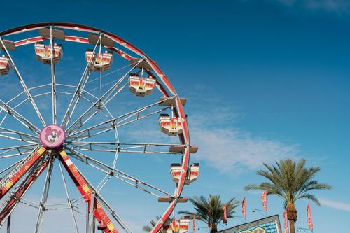 Ferris wheel at a fair against a bright blue sky, with palm trees and colorful gondolas