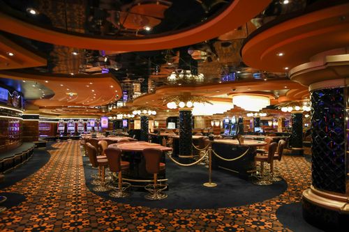 Elegant casino floor with roulette tables, slot machines, and warm amber lighting