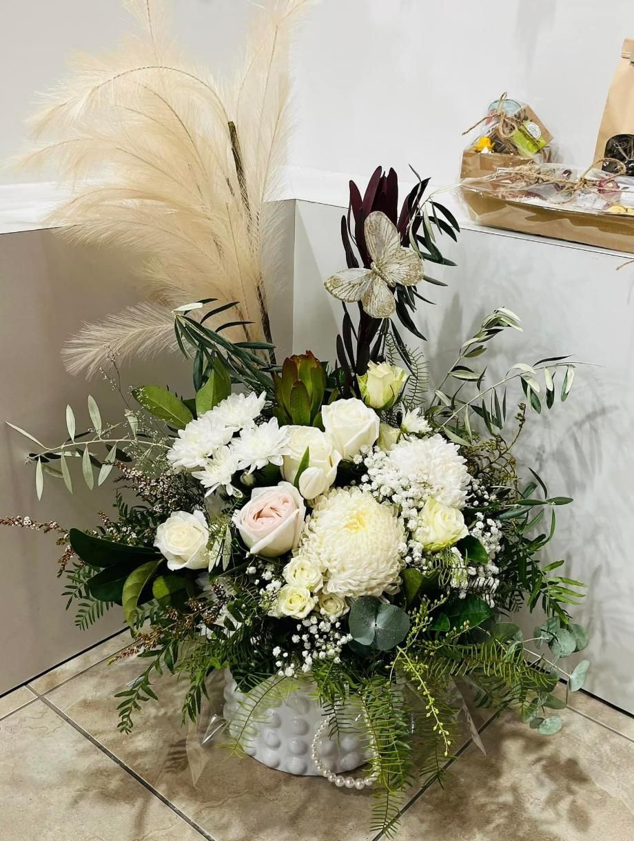 A Vase Filled With White Flowers and Greenery is Sitting on a Tiled Floor — Flower Hunt in Robina, QLD
