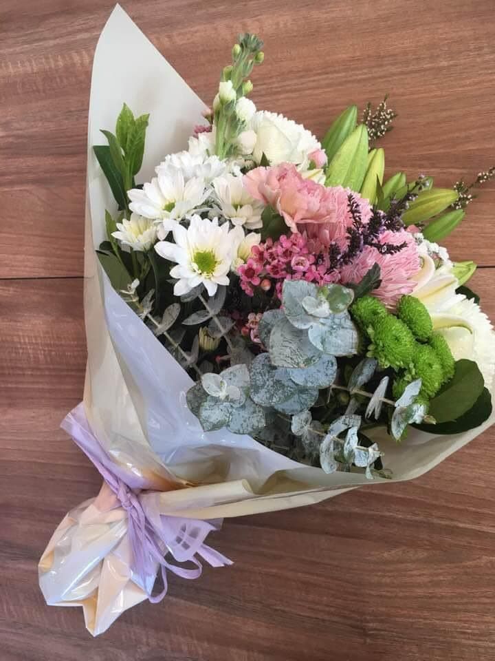 A Bouquet of Flowers Wrapped in White Paper is Sitting on a Wooden Table — Flower Hunt in Robina, QLD