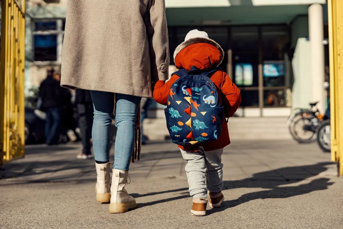 Adult and child walking toward a building, child in orange coat and blue backpack