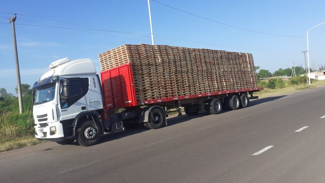 Un camión semirremolque blanco transporta una larga plataforma roja cargada de cajas de madera apiladas en una carretera.
