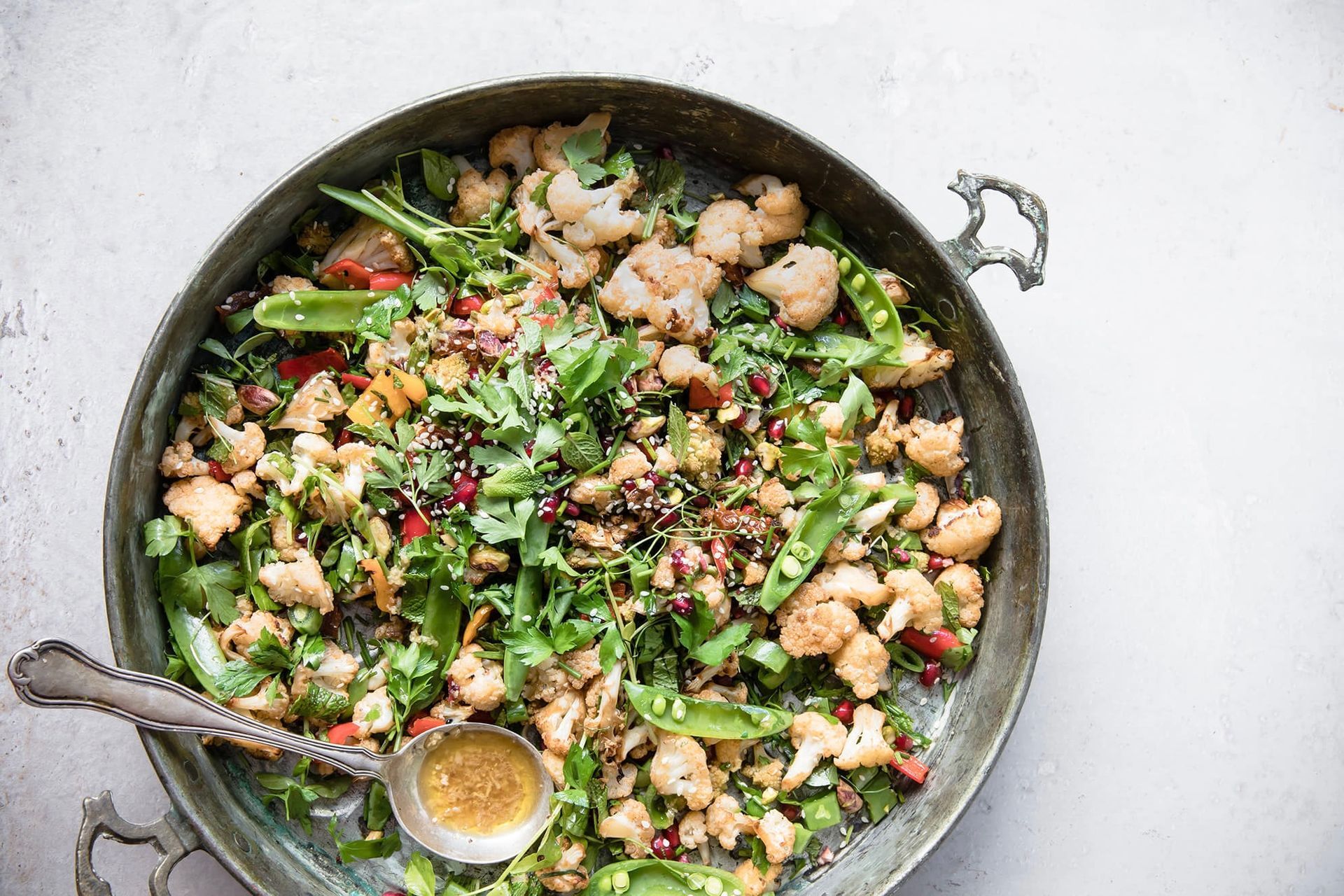 Overhead view of a skillet with shrimp, chopped vegetables, herbs, and a spoon on a light surface