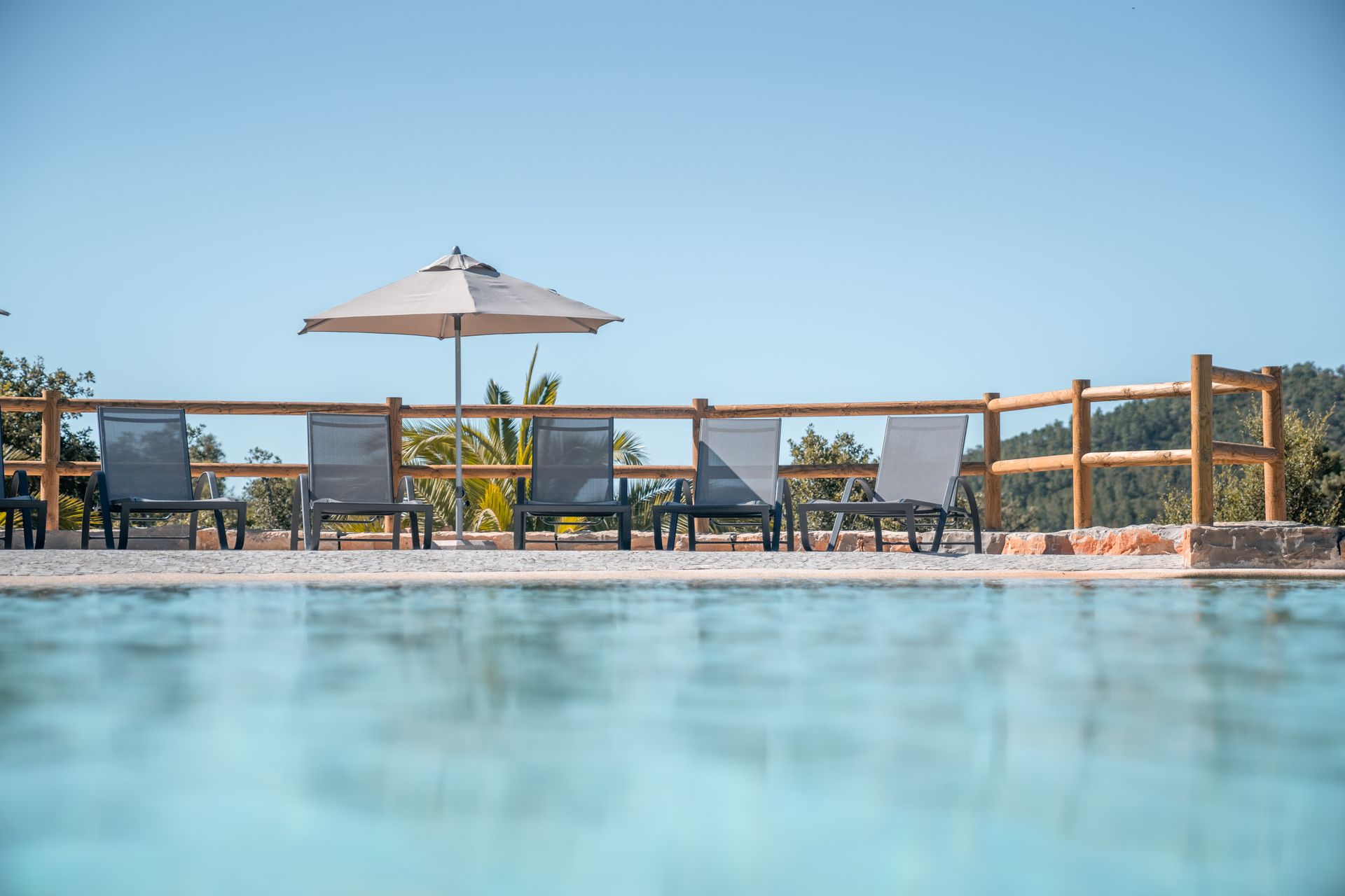 Poolside lounge chairs and umbrella beside a calm blue swimming pool under a clear sky