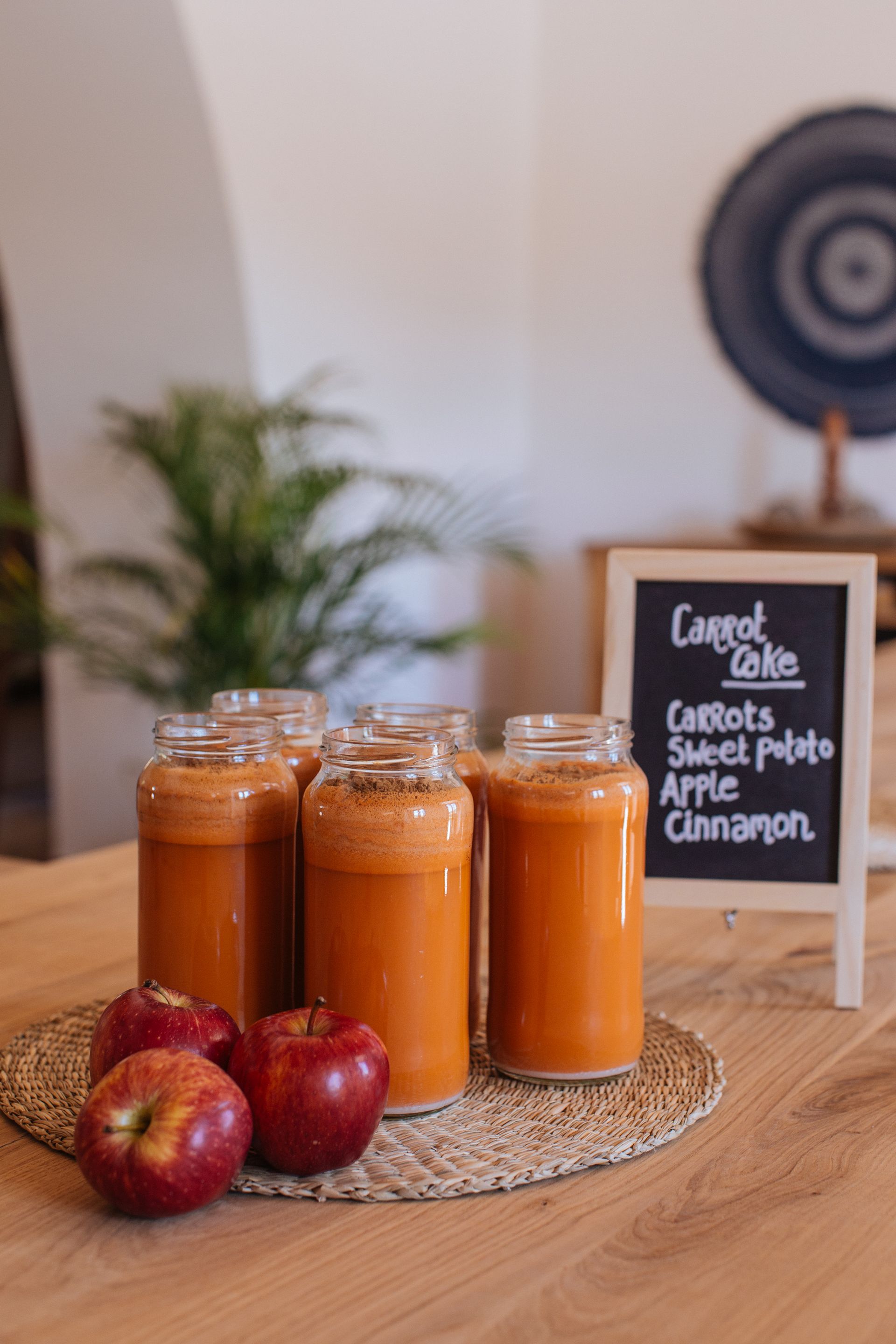 Three jars of orange preserves on a table with apples and a small chalkboard label
