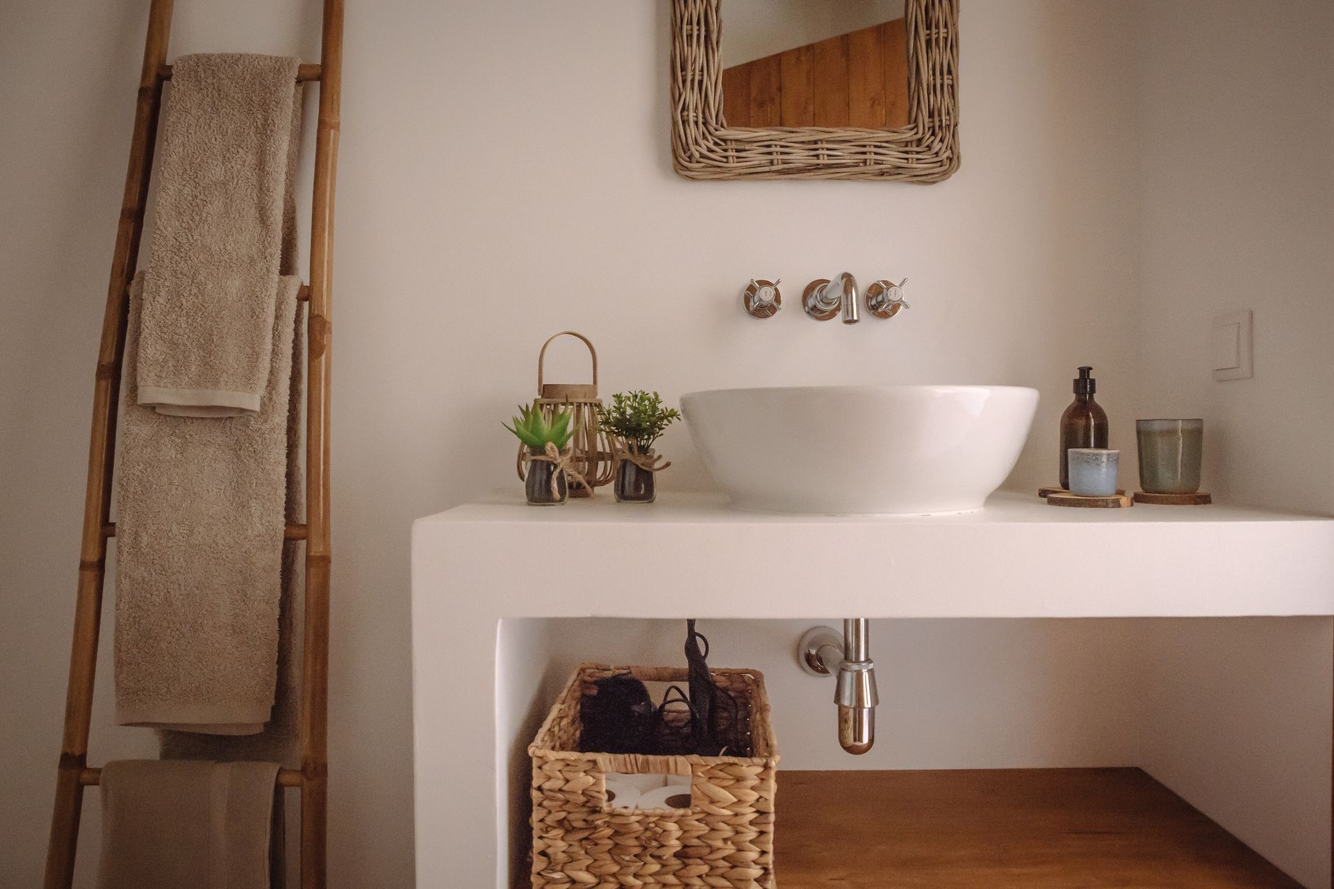 Modern bathroom vanity with white vessel sink, woven baskets, and towels on a ladder rack