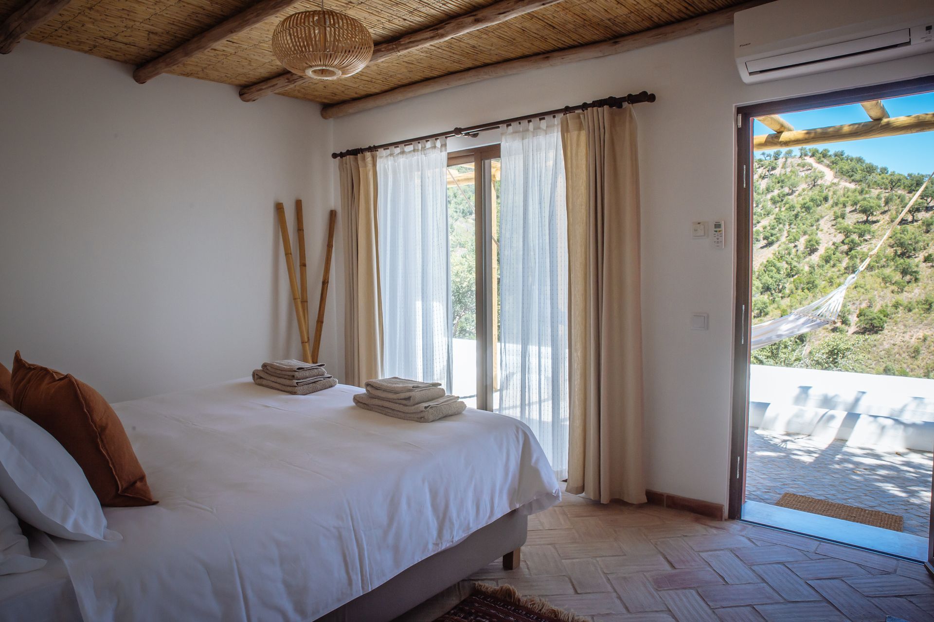 Cozy bedroom with a bed, sliding glass doors, and a balcony overlooking green hills and water