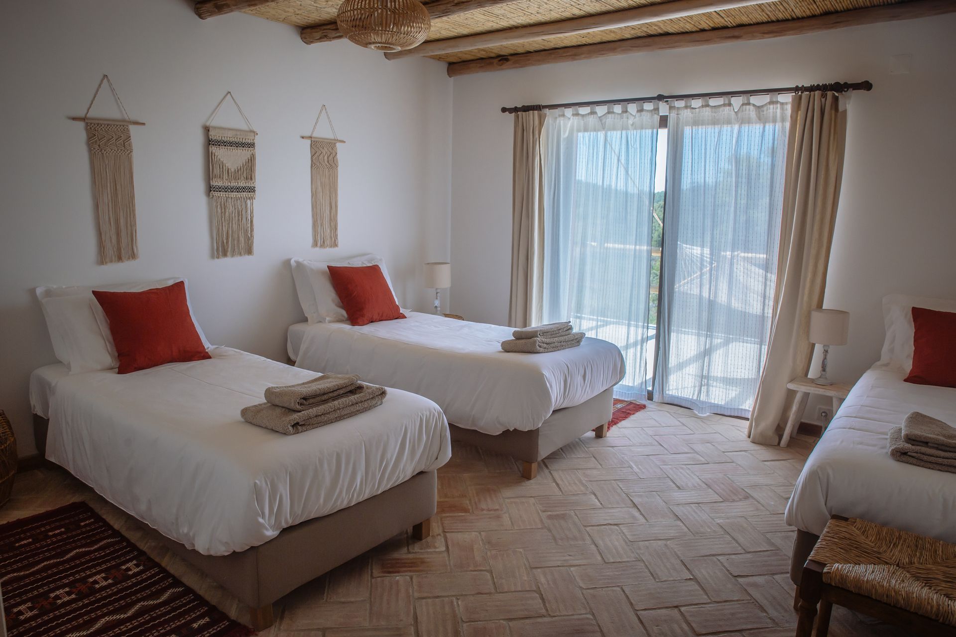 Bright bedroom with four twin beds, red pillows, and sliding glass doors to a balcony