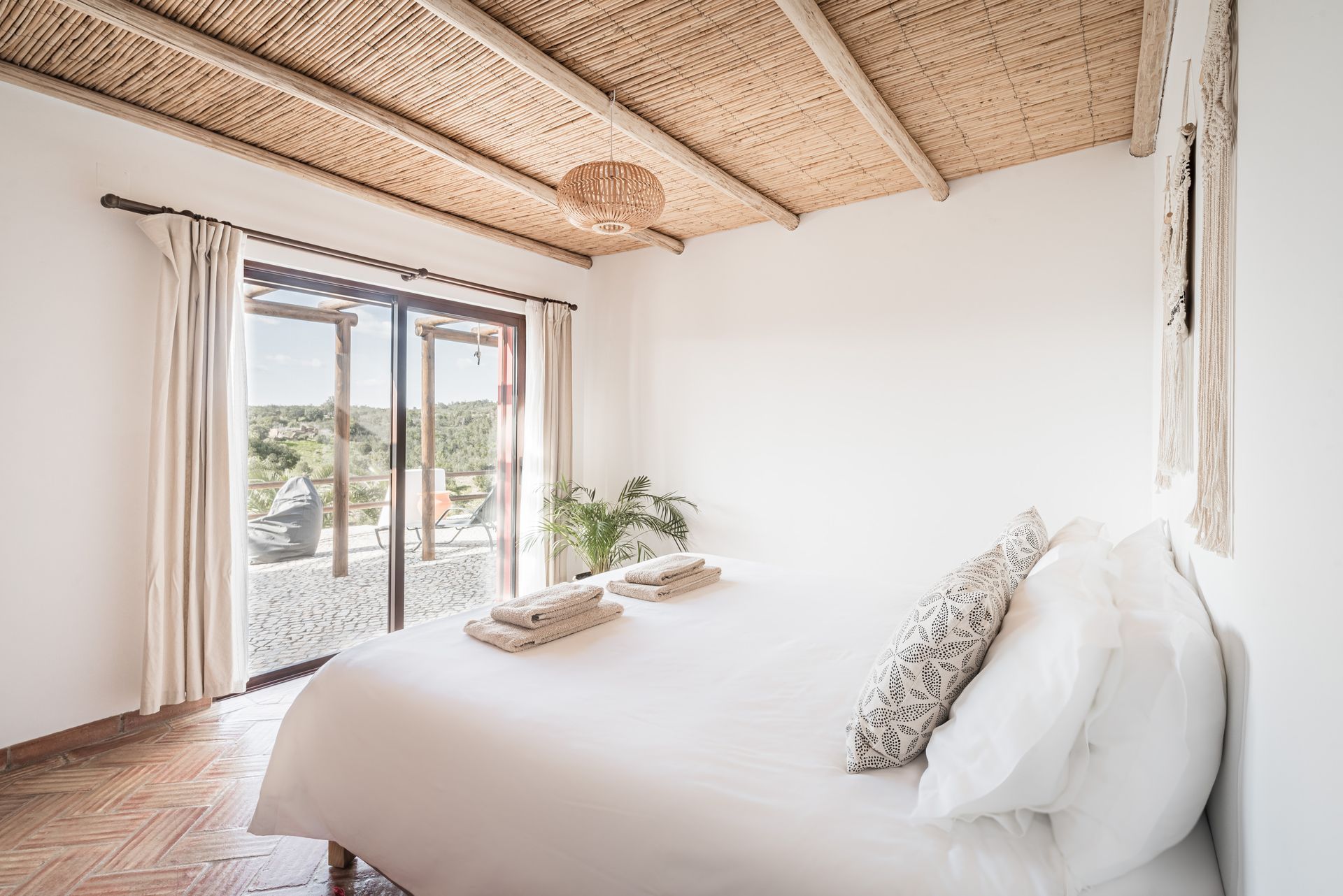Bright bedroom with a bed, woven ceiling, and sliding glass doors opening to a sunny patio