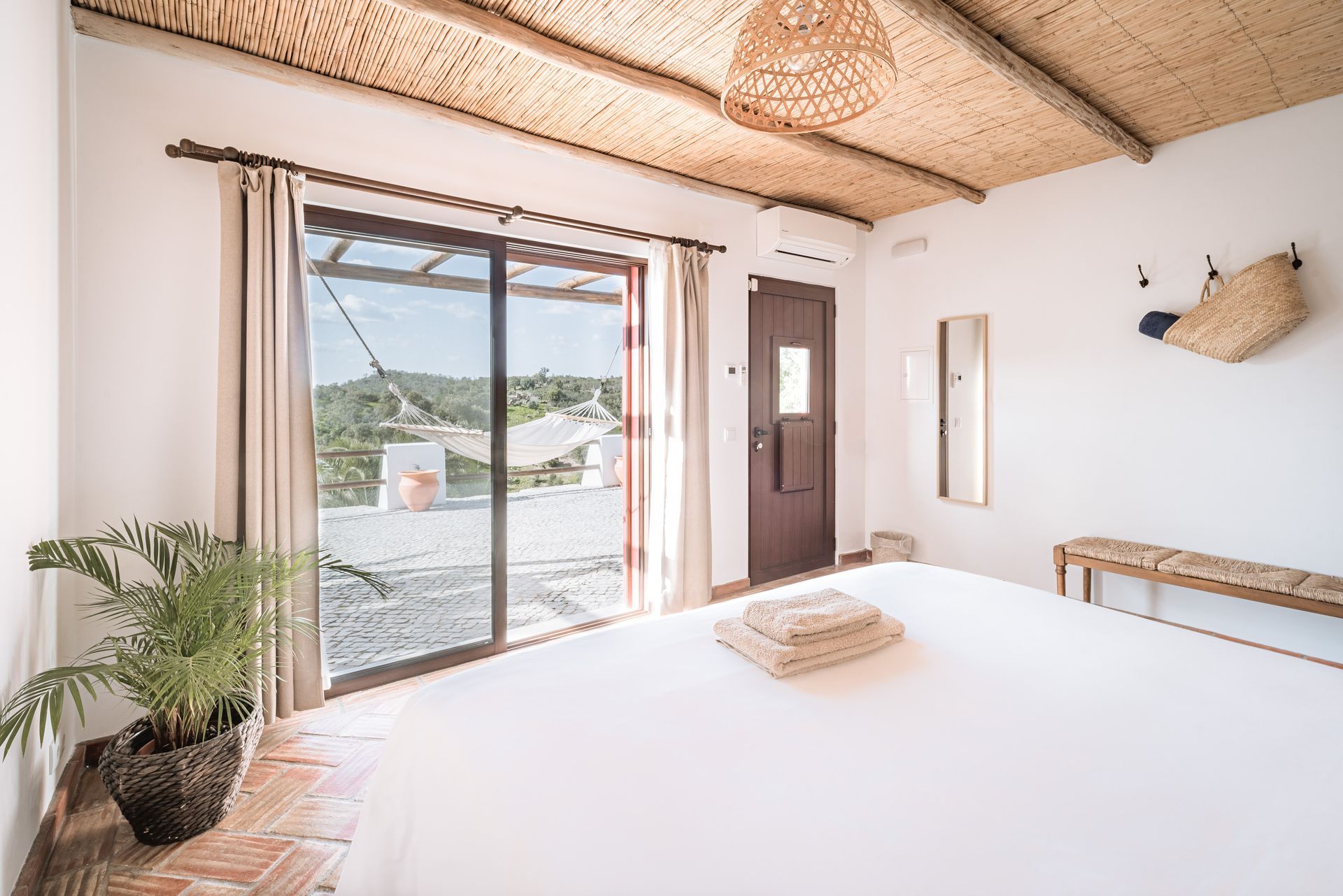 Bright bedroom with white bed, woven ceiling, sliding glass doors, and a view of the outdoors