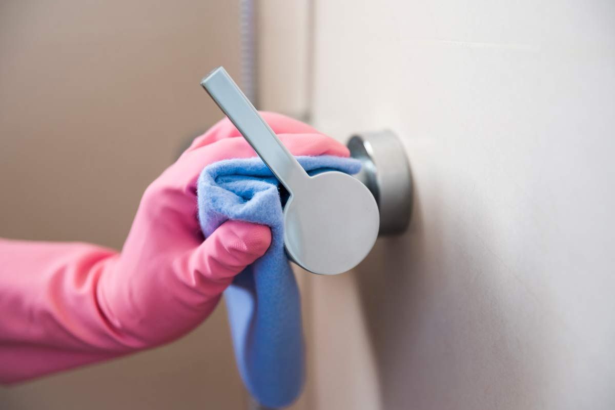 Cleaner disinfecting a high-touch door handle in a medical centre