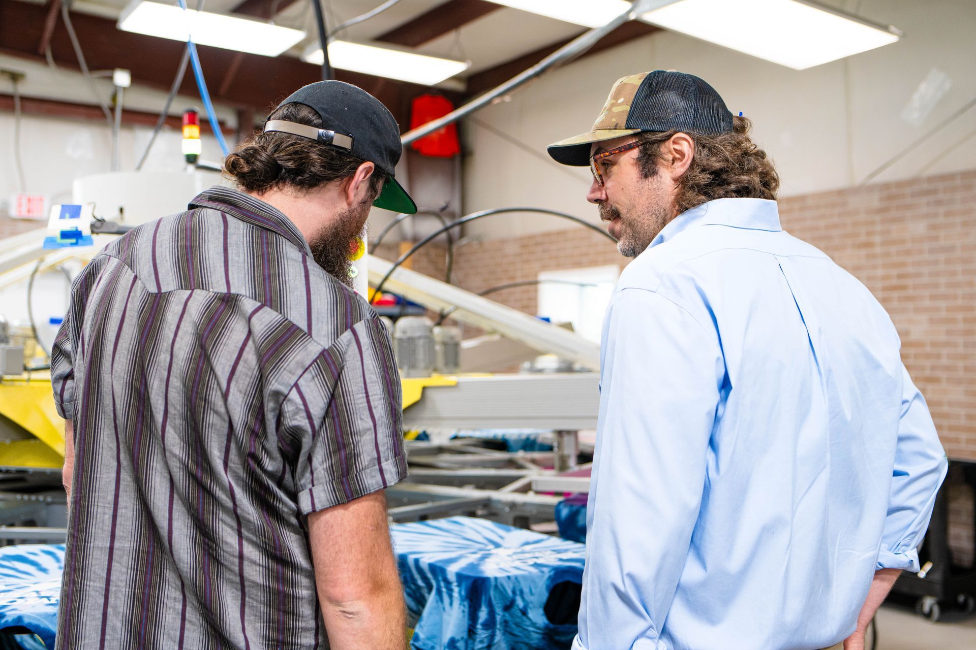 Two men are standing next to each other in a factory looking at a machine.