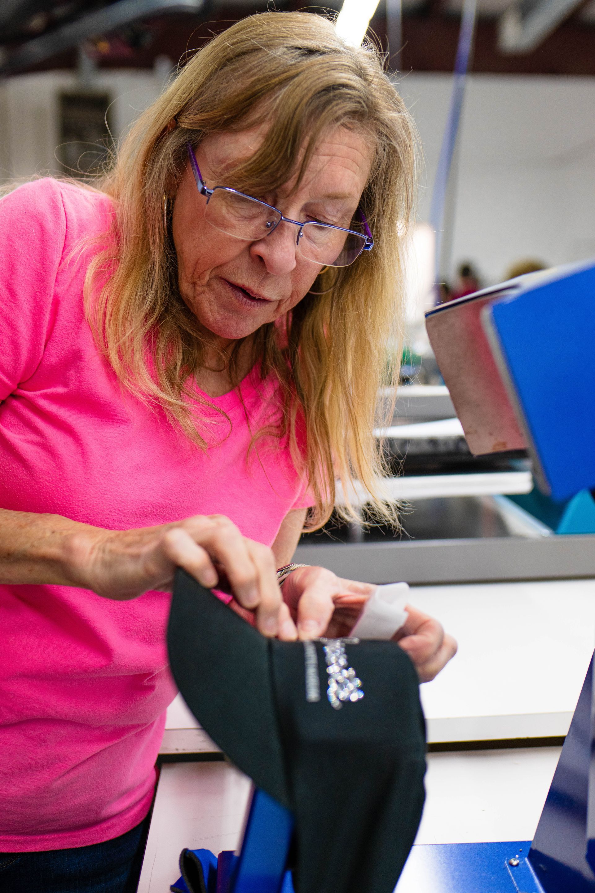 A woman in a pink shirt is working on a hat in a factory.
