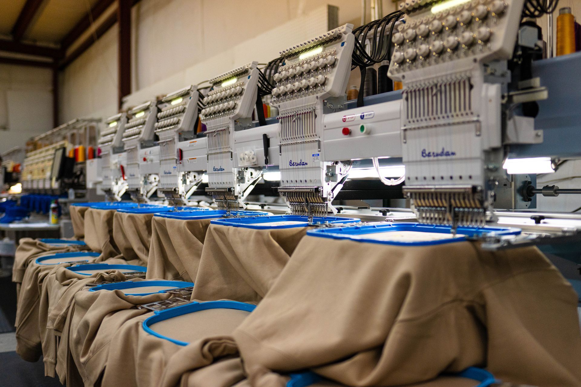 A row of embroidery machines are sitting in a warehouse.
