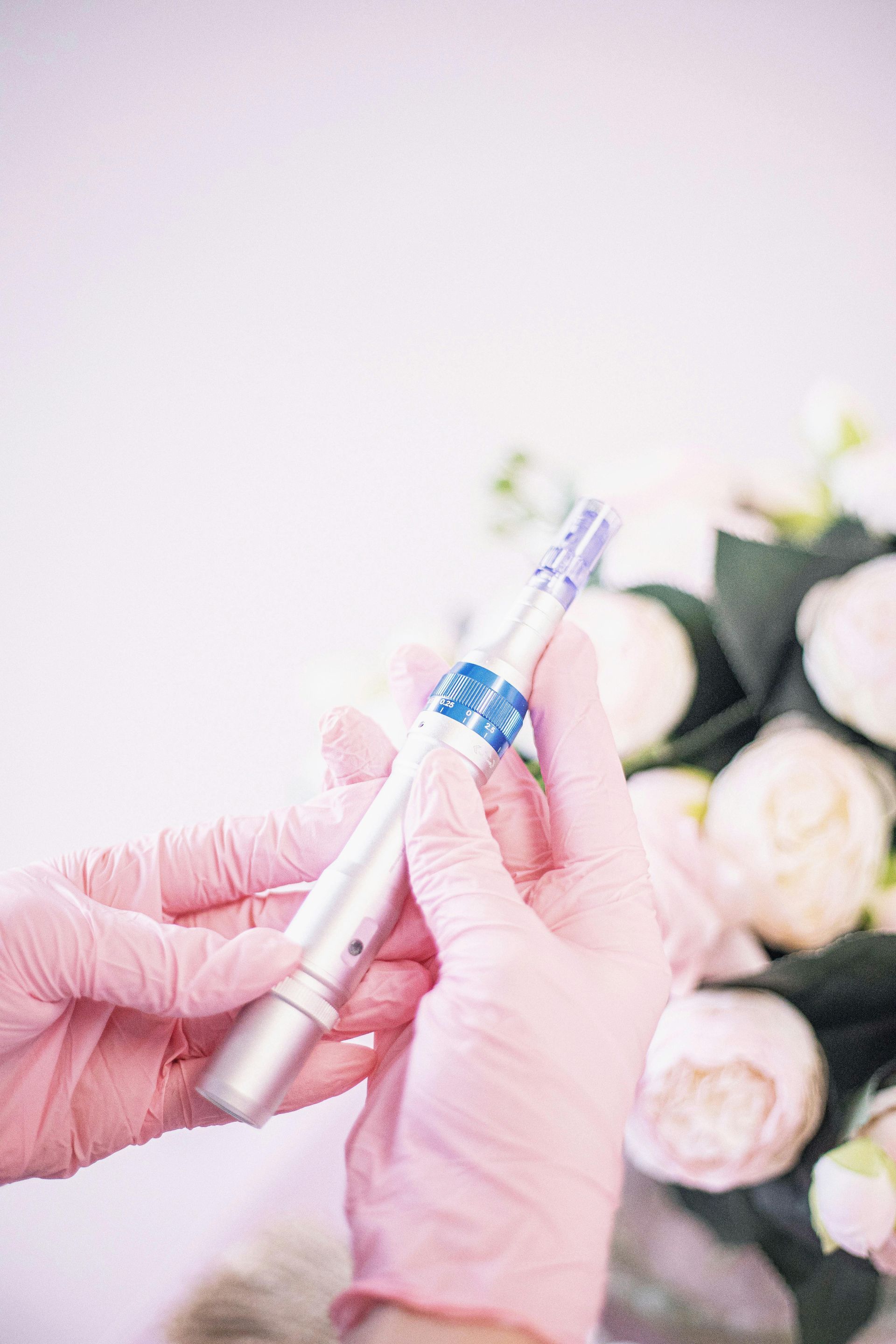 Gloved hands holding a dental syringe near white roses on a soft pink background
