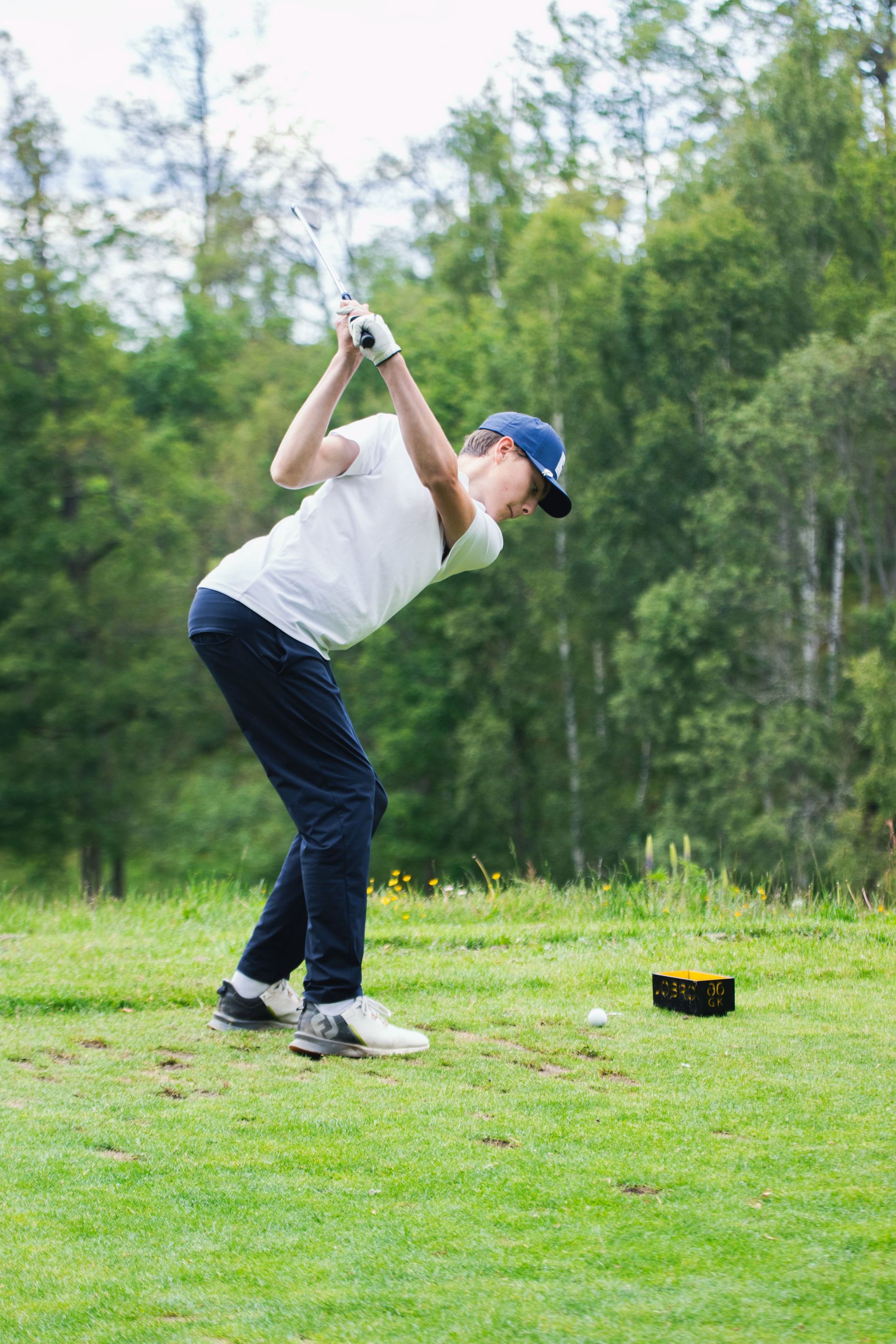 Golfer mid-swing on a green course, with a tee and ball nearby