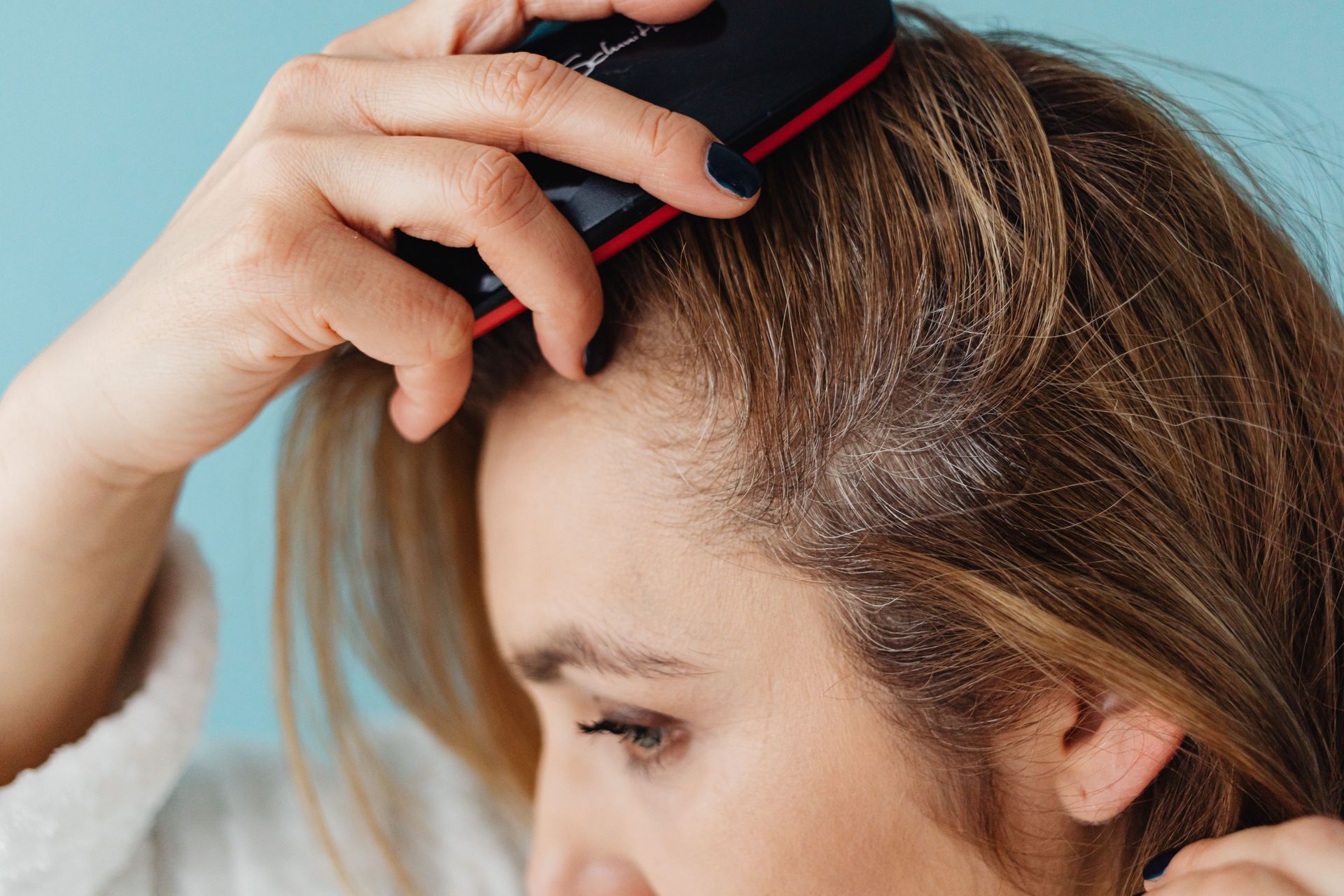 Woman using a black comb to part her brown hair close-up