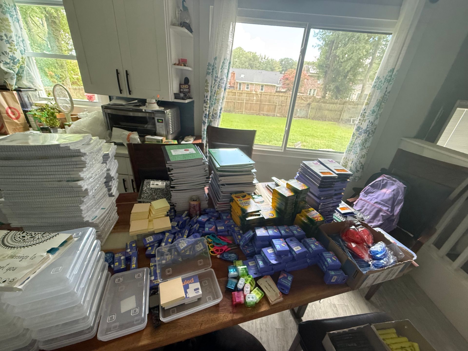 Kitchen table covered with stacked snacks, plastic containers, and papers by a bright window