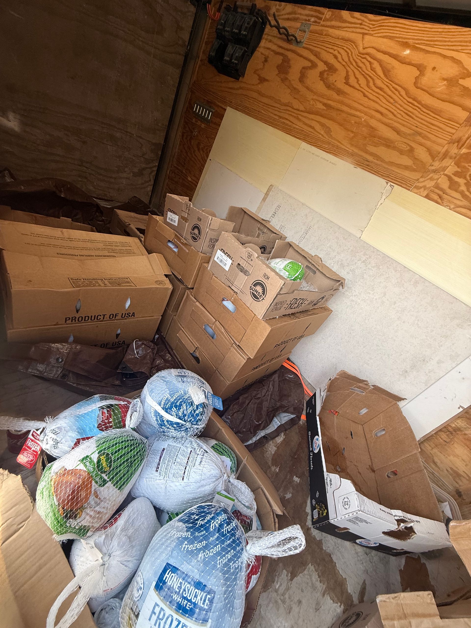 Cluttered storage area with cardboard boxes, bags, and household items scattered on the floor.