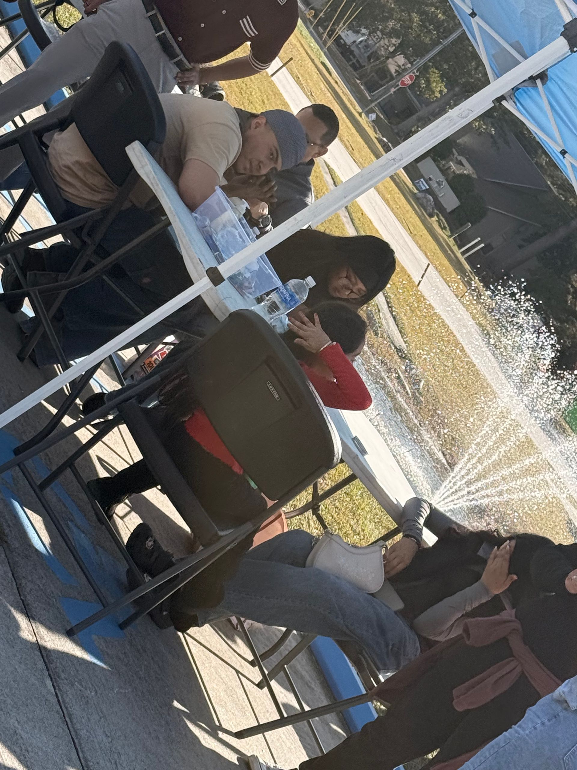 People seated at an outdoor café under blue umbrellas, chatting around tables in sunlight