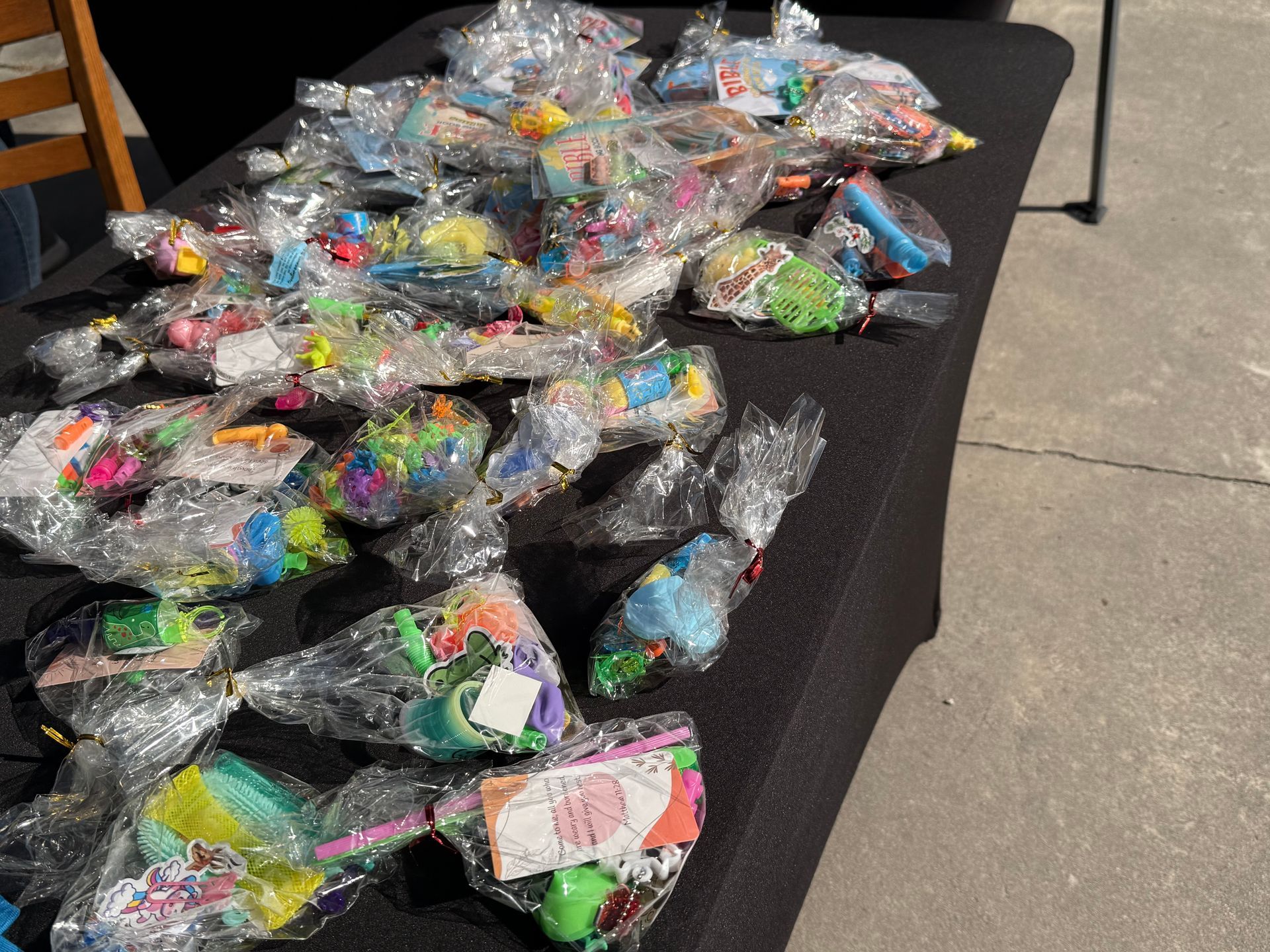 Stacked clear-bagged toys or prizes on a black table beside a concrete floor.