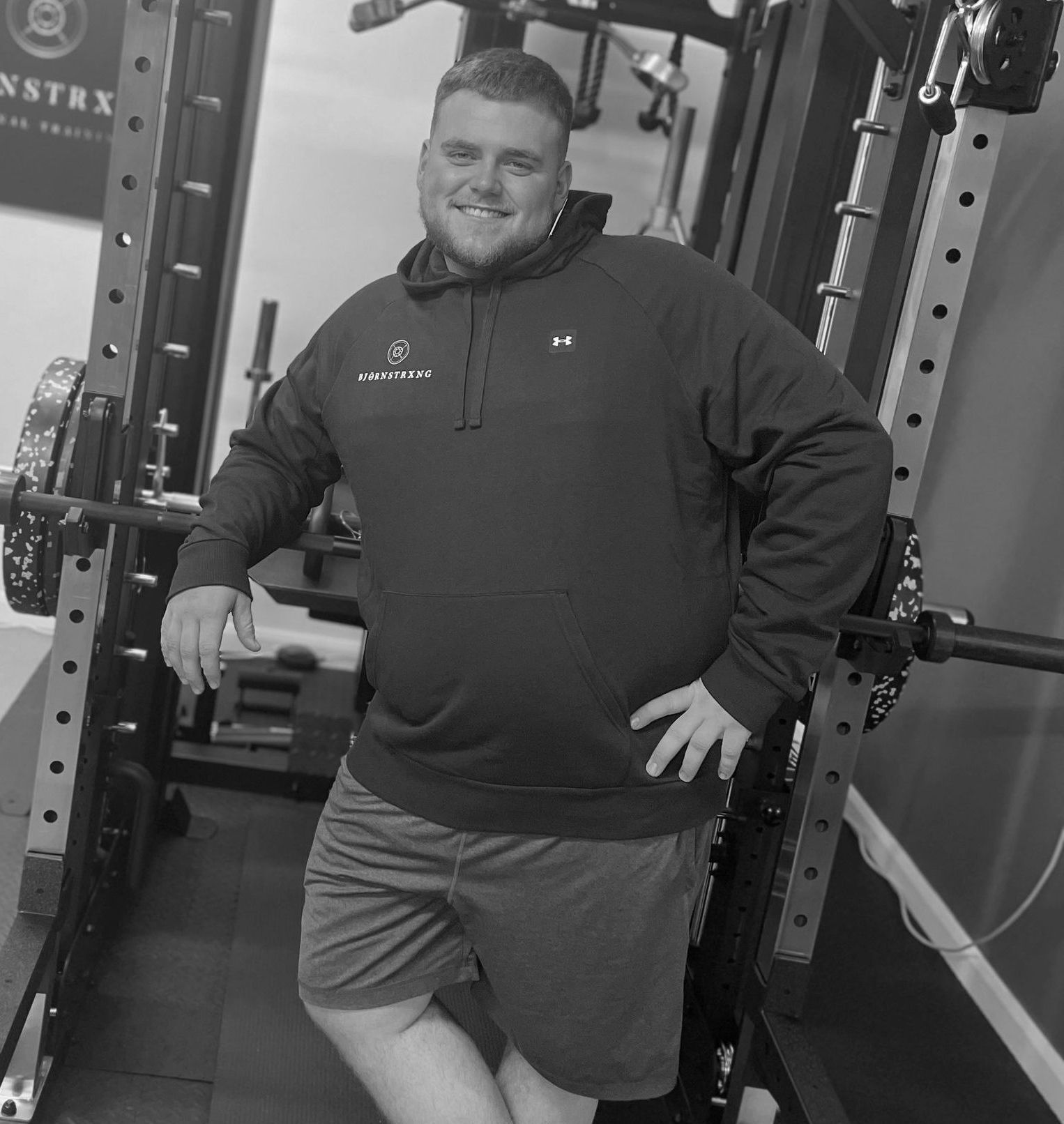 Man in workout clothes smiles, leaning on gym equipment.