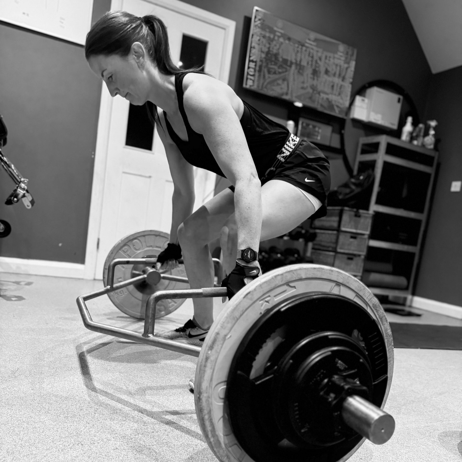 Person deadlifting a barbell in a gym, viewed from low angle.