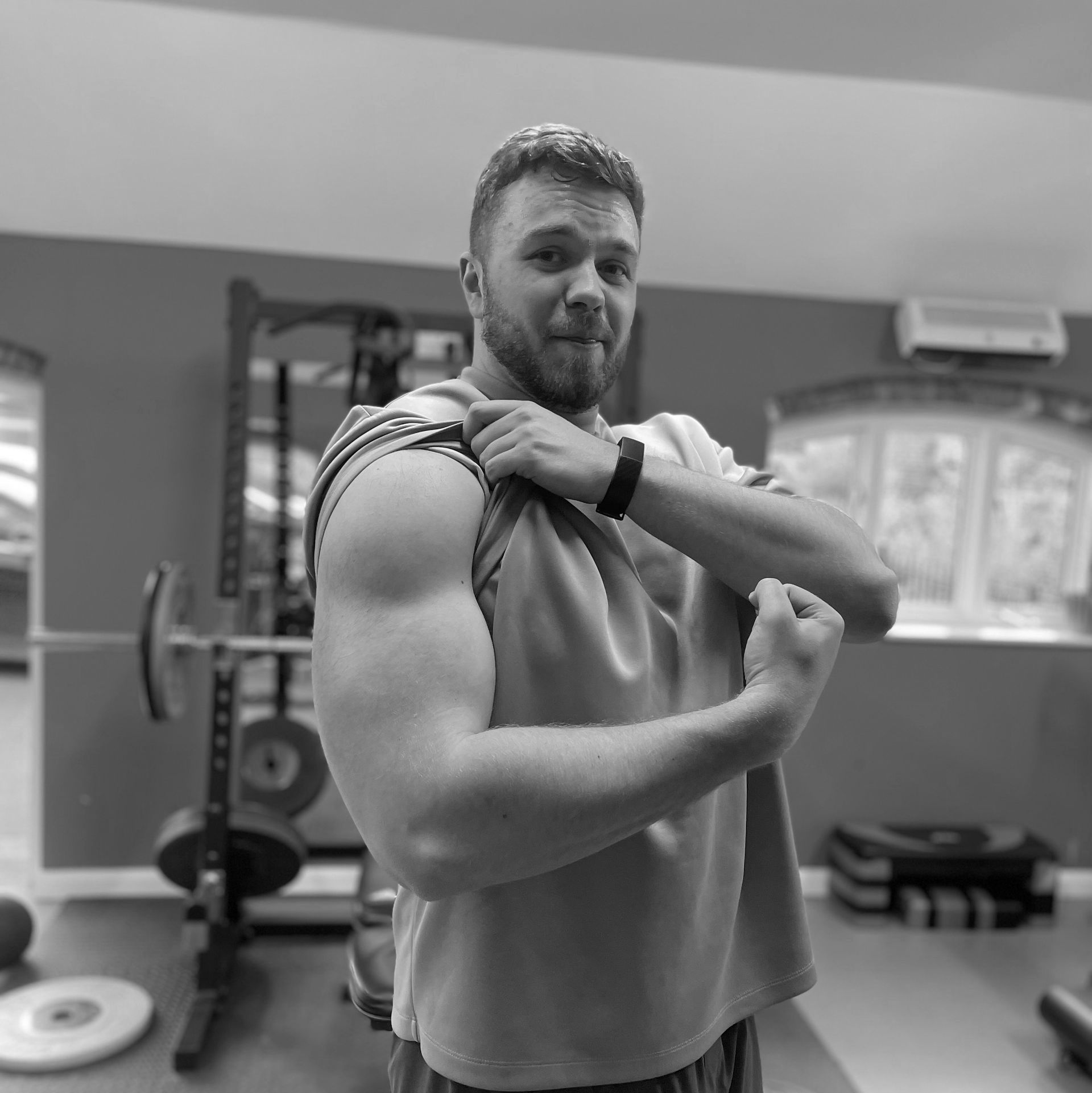 Man flexing bicep in home gym, weight rack and equipment visible in the background.