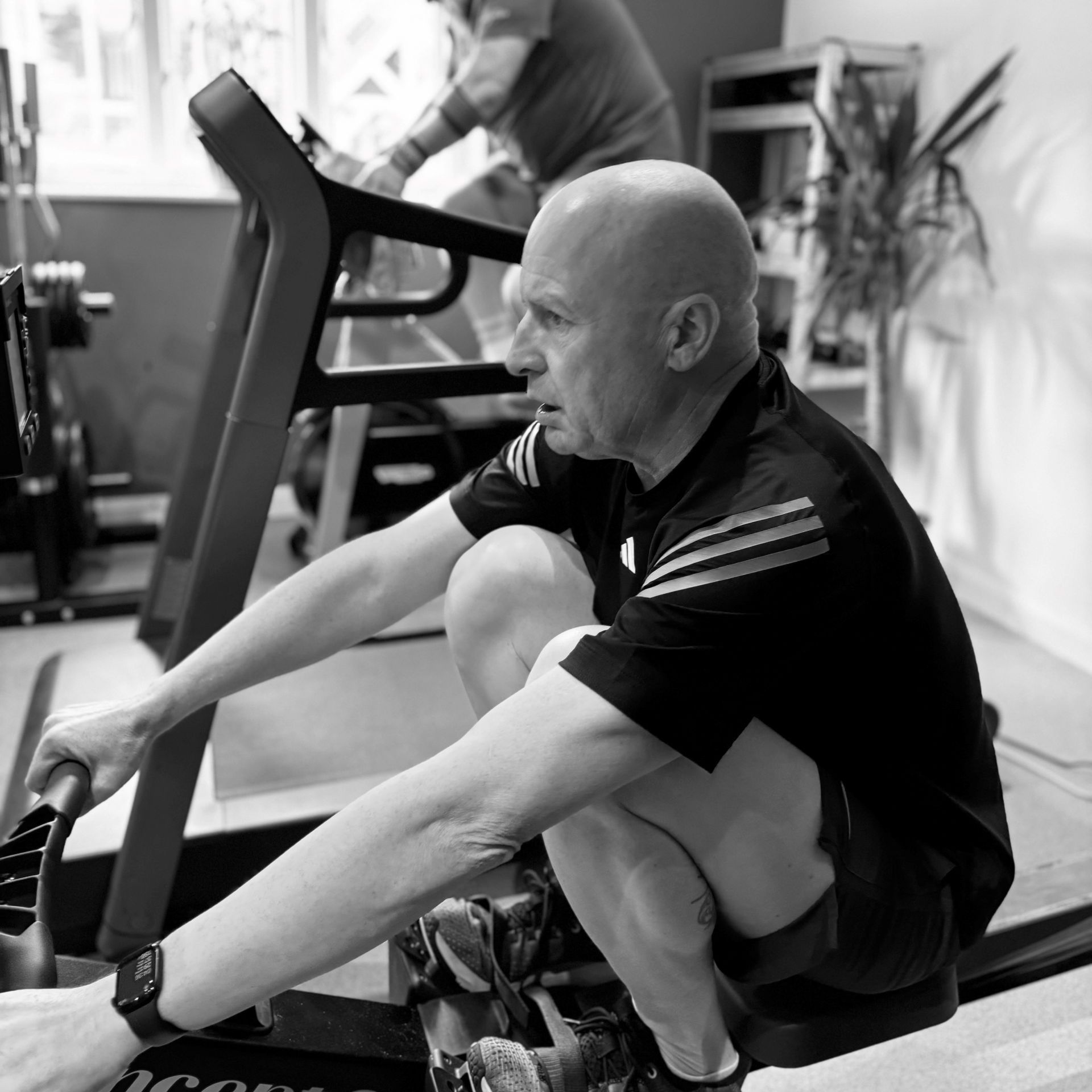 Man on rowing machine in gym, treadmill and person in background.
