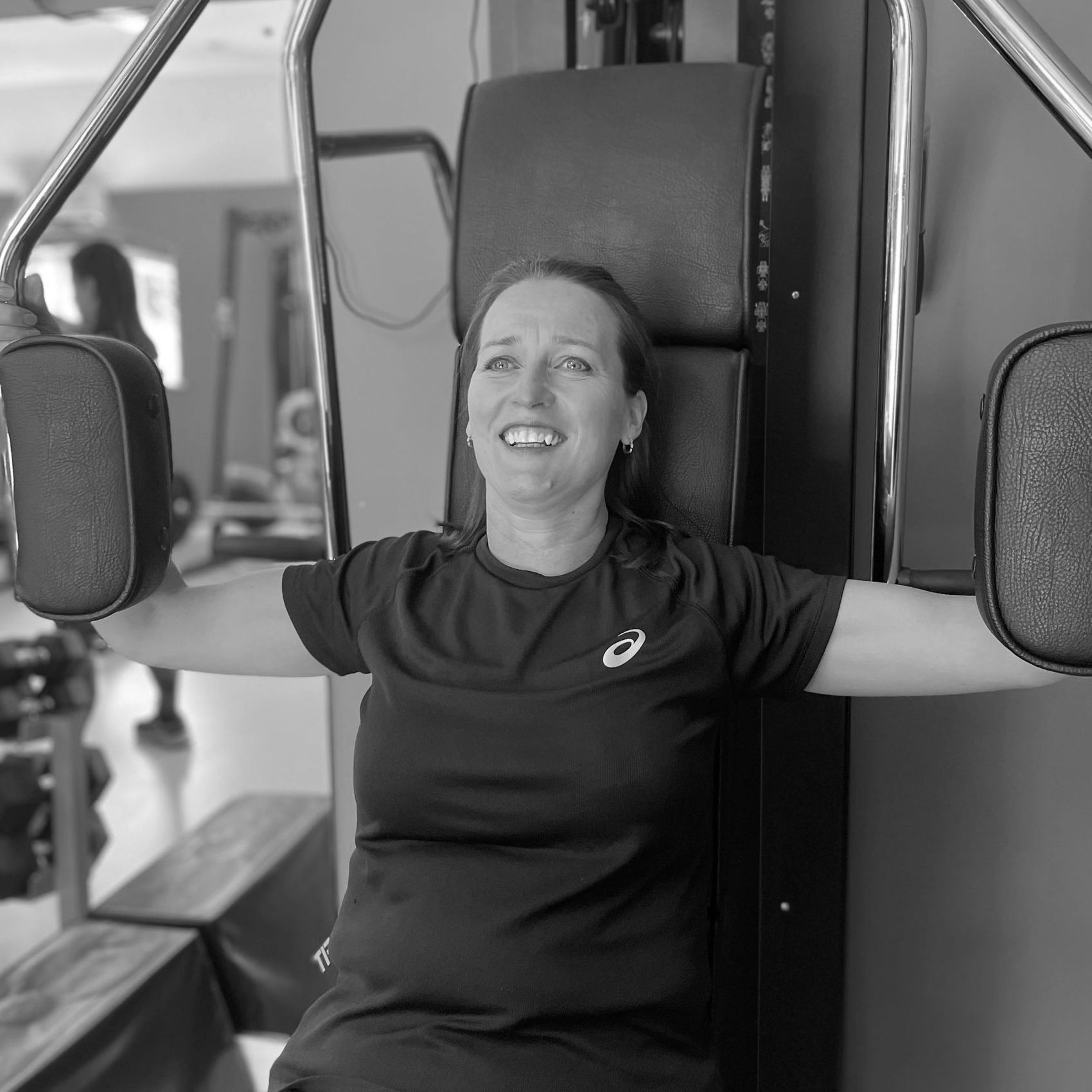 Woman using a chest press machine at a gym, smiling.