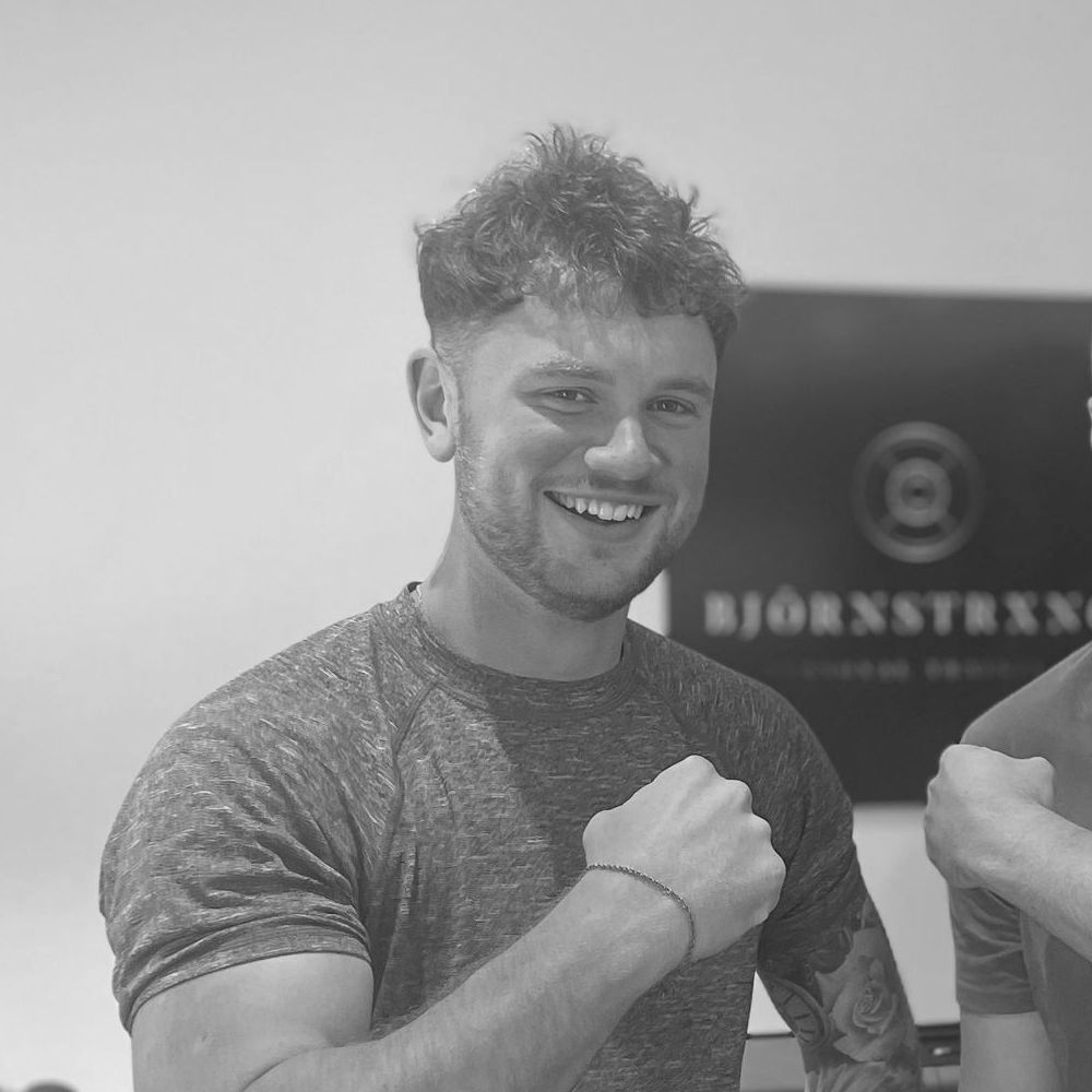 Smiling man with a fist pump, wearing a gray shirt, in front of a logo.
