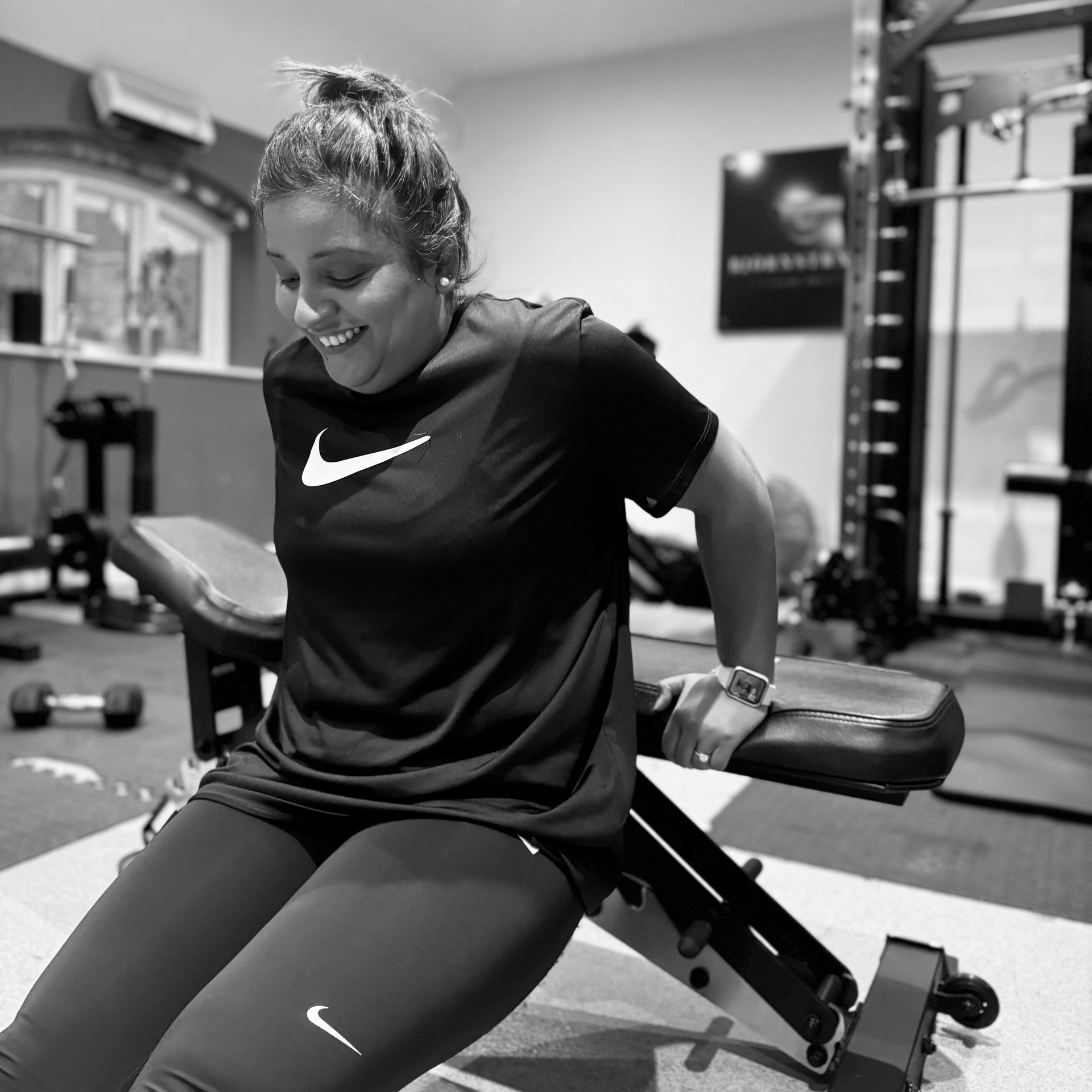 Woman smiles while doing tricep dips on a weight bench in a home gym.