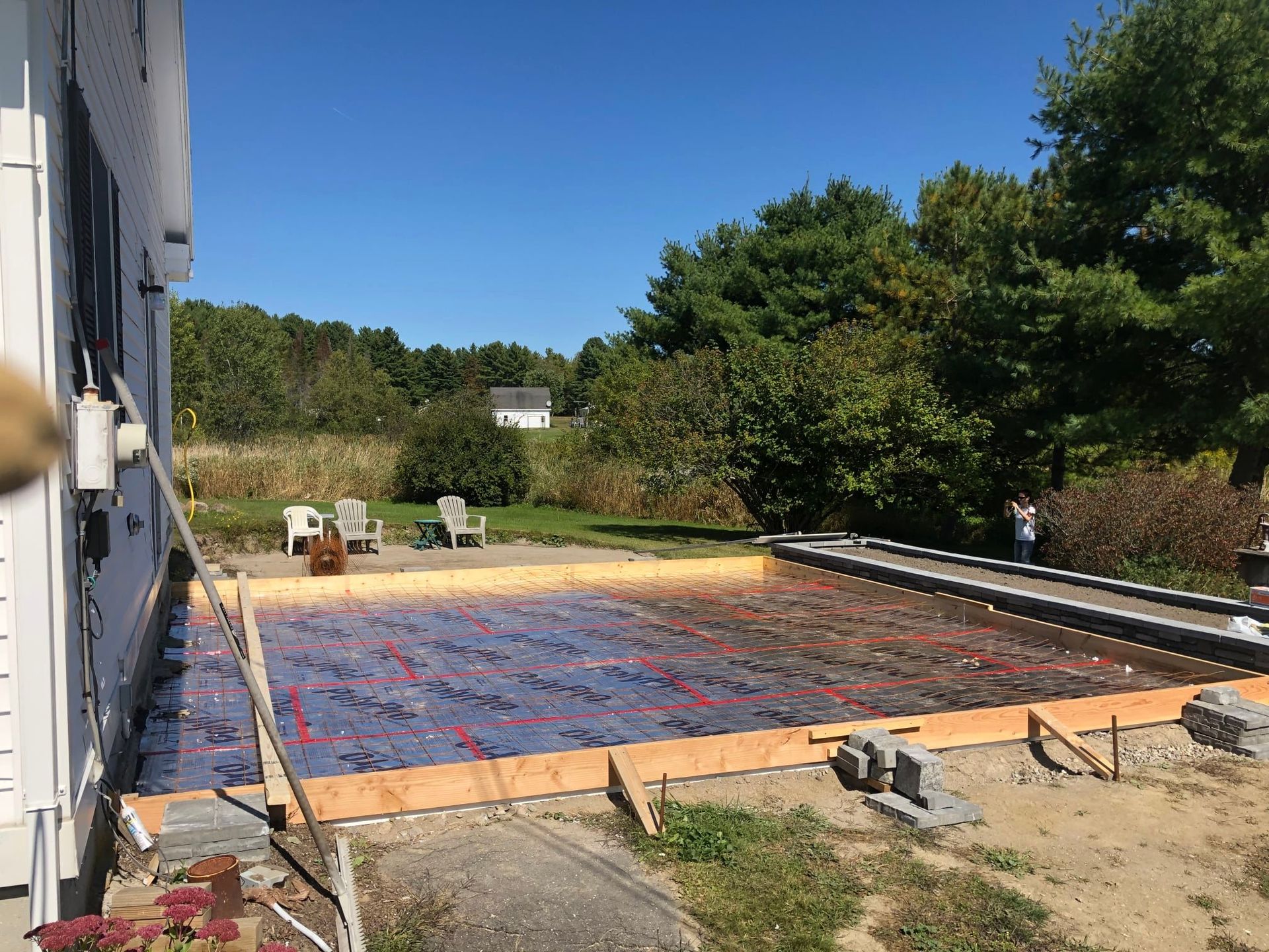 Construction site, outdoor. Patio foundation framed with wooden boards, rebar grid, blue insulation. Sunny day.