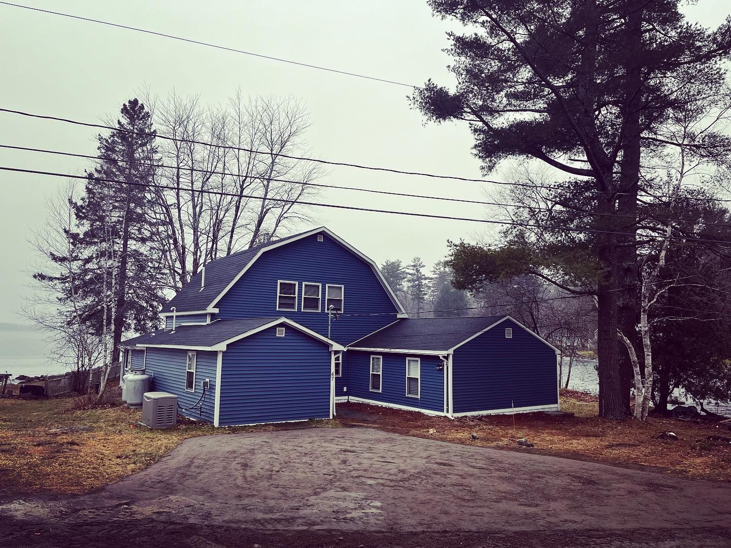 Blue house with white trim, near a body of water, under a cloudy sky.