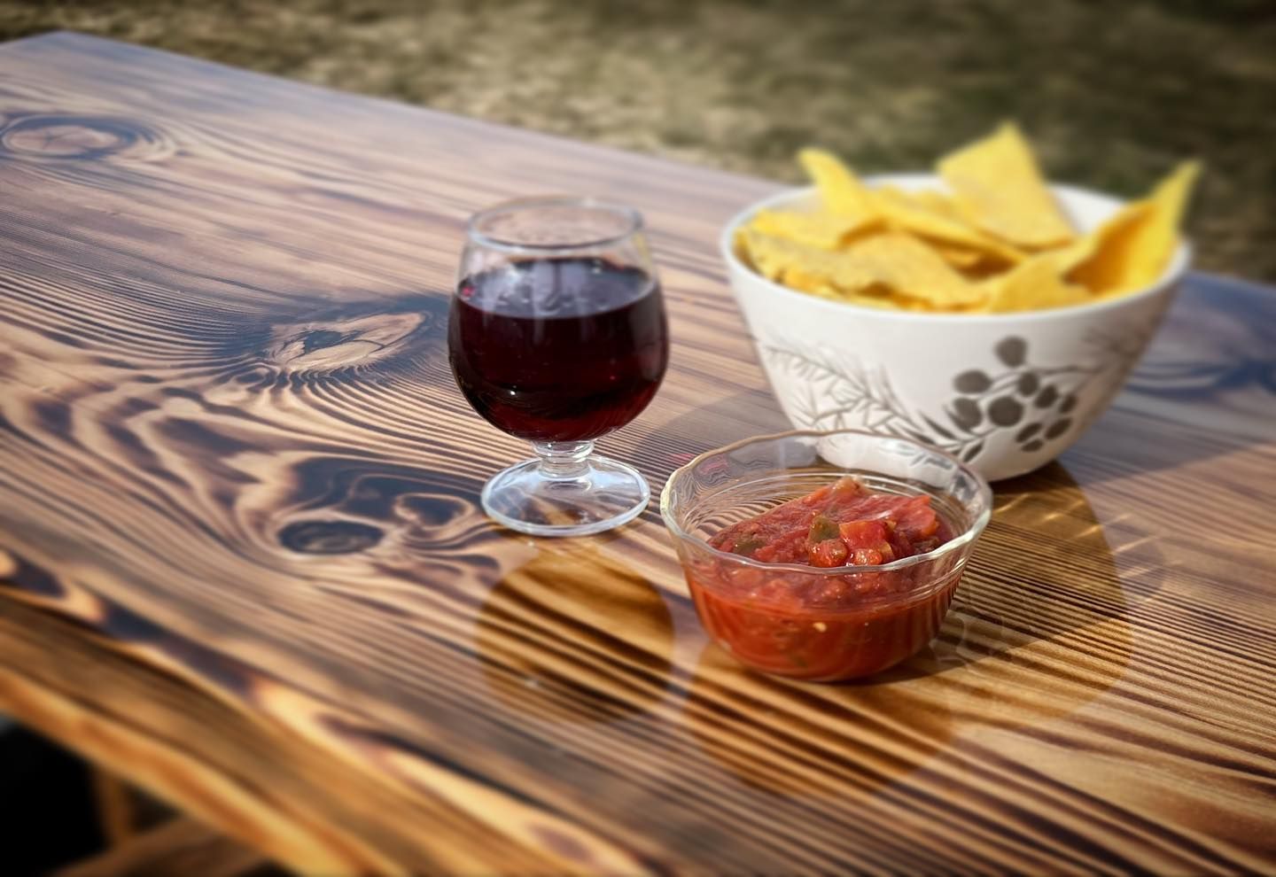 Glass of red wine, salsa, and tortilla chips on a wooden table.