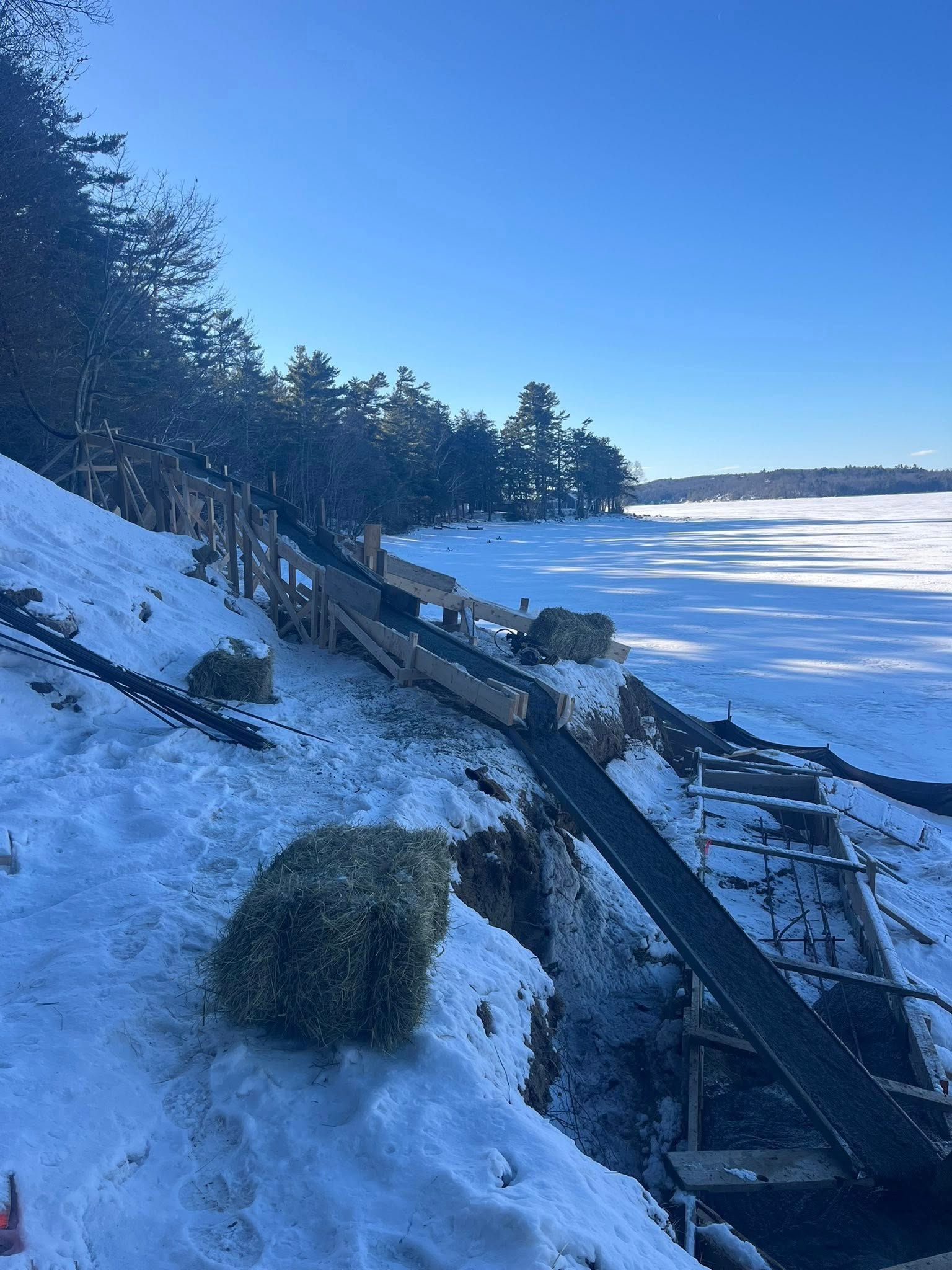 Wooden ramp and stairs on a snowy hillside leading towards a frozen lake.