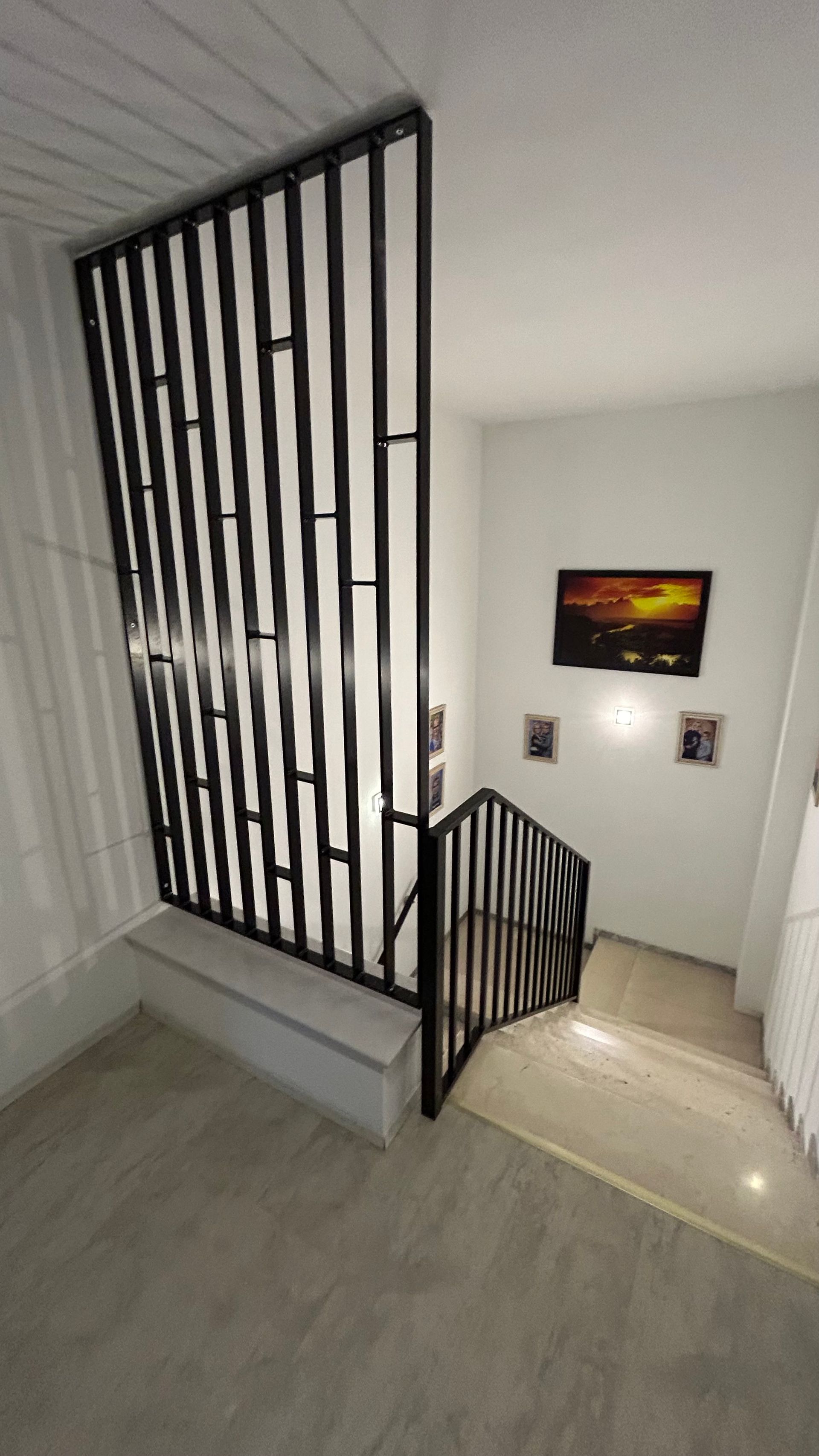 Interieur mit schwarzem Metalltreppengeländer und Wandpaneel; Kunstwerke an weißen Wänden.