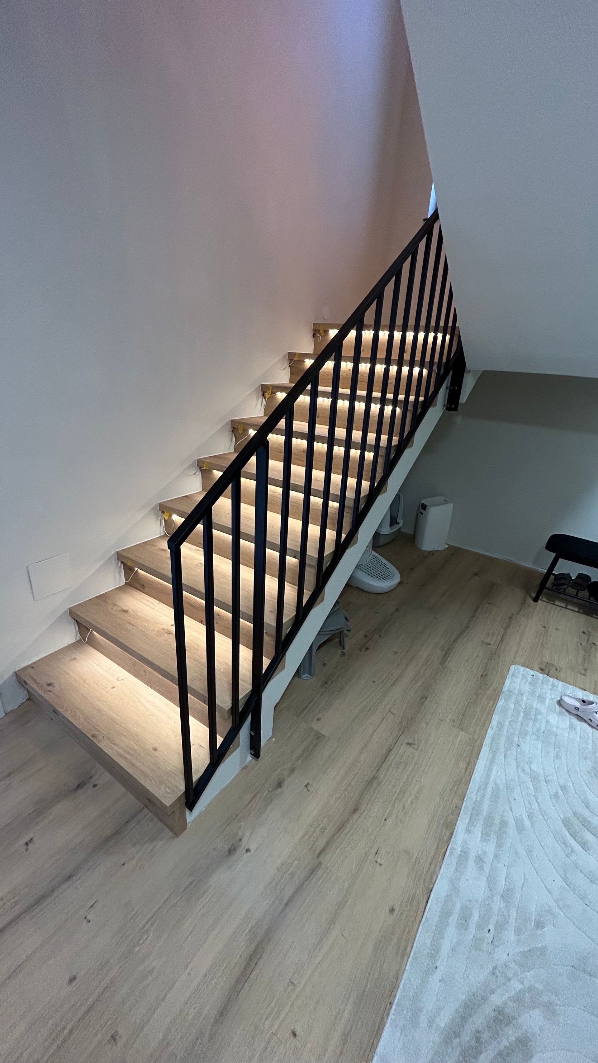 Holztreppe mit schwarzem Geländer und Stufenbeleuchtung.