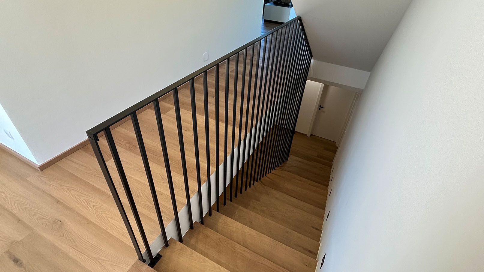 Holztreppe mit schwarzem Geländer und weißen Wänden.
