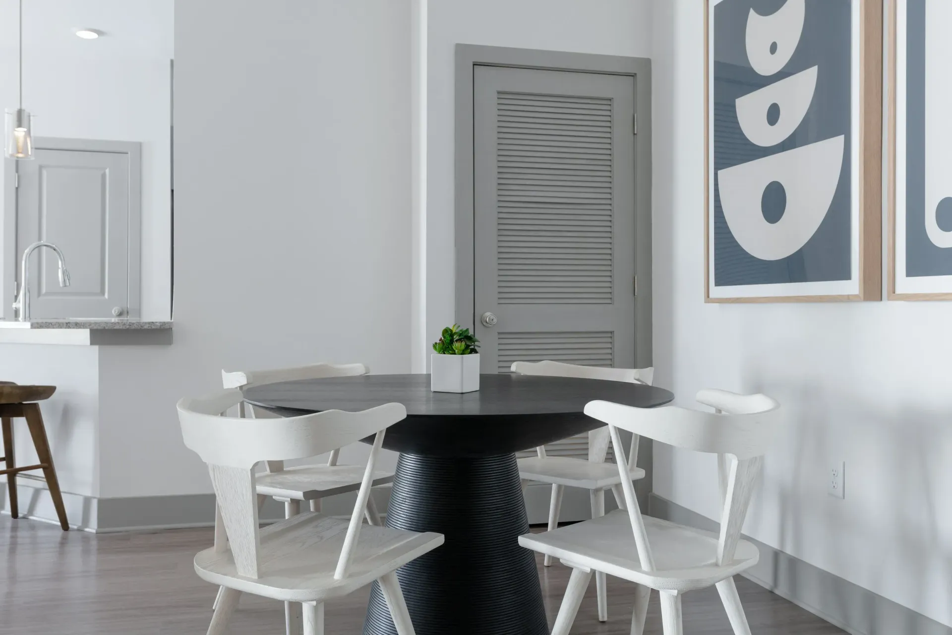Interior dining area with a round black pedestal table, white chairs, a small plant, and gray door.