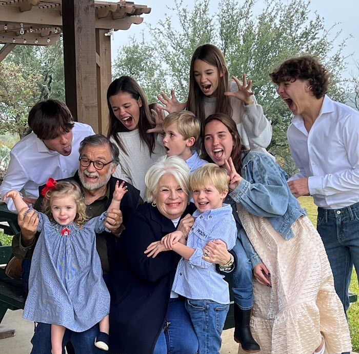 A group of people of various ages posing outdoors, laughing and making silly faces while gathered around two elders.